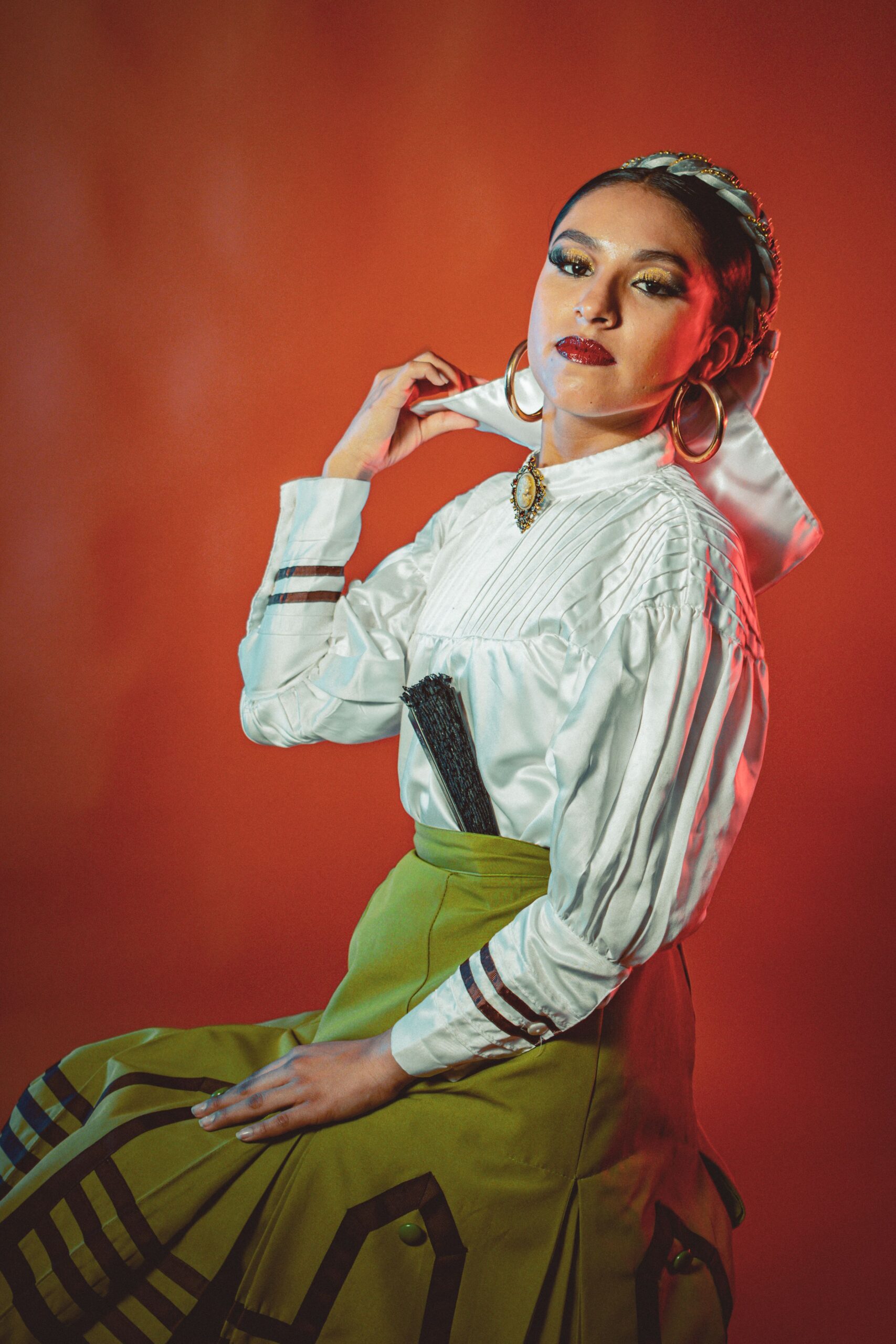Elegant woman in traditional Mexican attire posed against a vibrant background, showcasing cultural fashion.